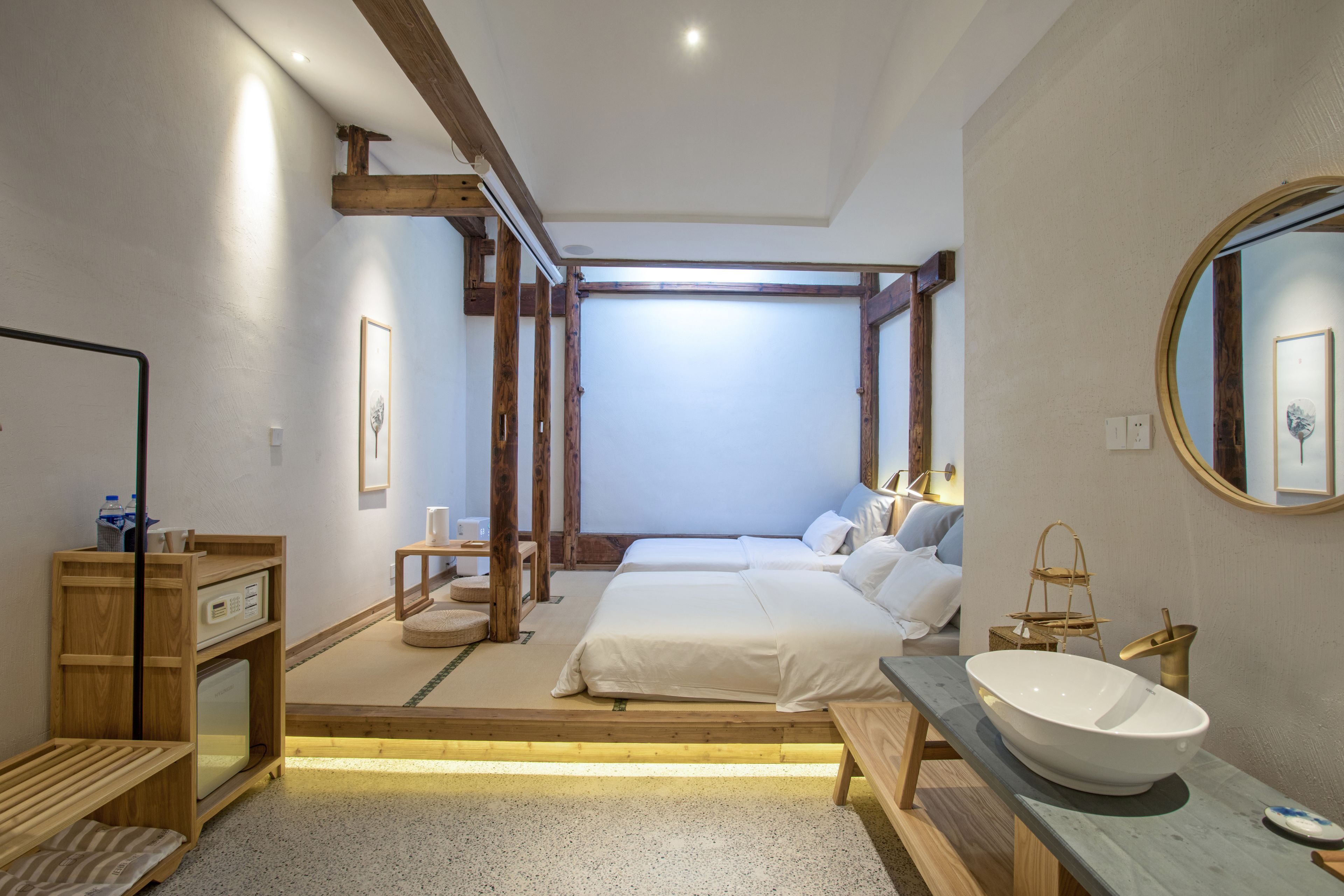 Un dormitorio con una cama grande, mesitas de noche, un banco de madera, un espejo amplio y un lavabo blanco.