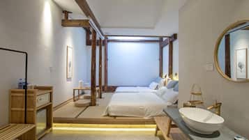 Un dormitorio con una cama grande, mesitas de noche, un banco de madera, un espejo amplio y un lavabo blanco.