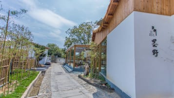 Un sendero lleva a un edificio con tejado de madera y fachada blanca. Hay un letrero con caracteres japoneses en la pared.