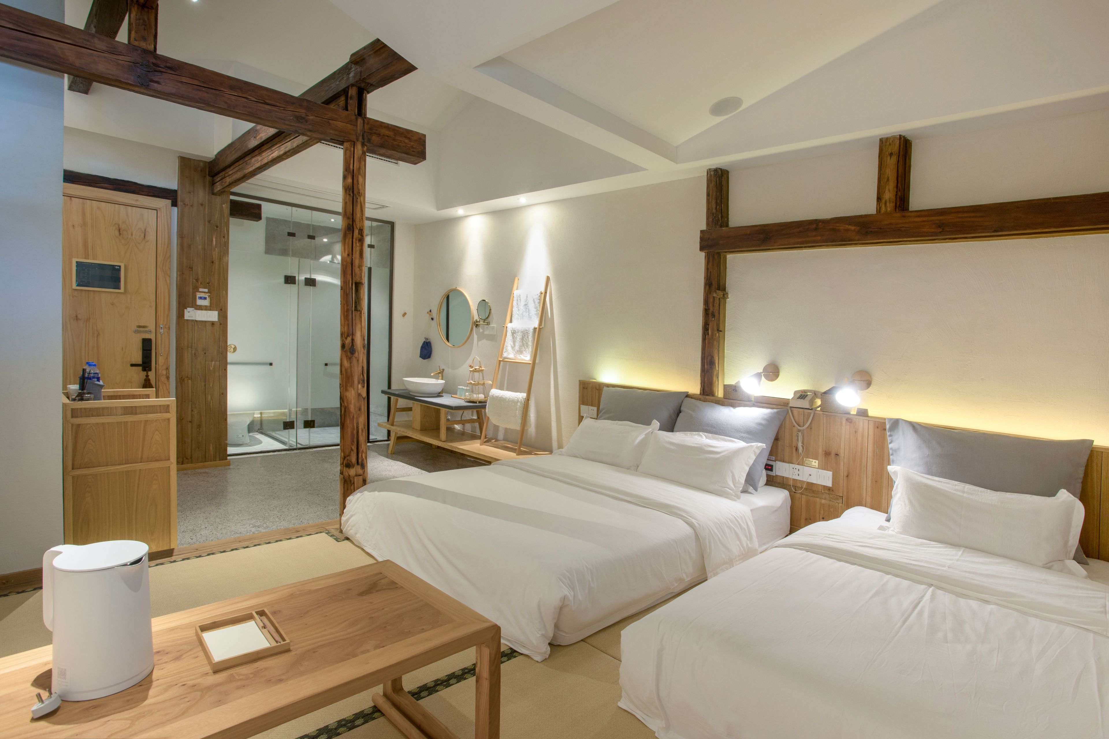 A hotel room with two beds, a wooden desk, a mirror, and a small table.