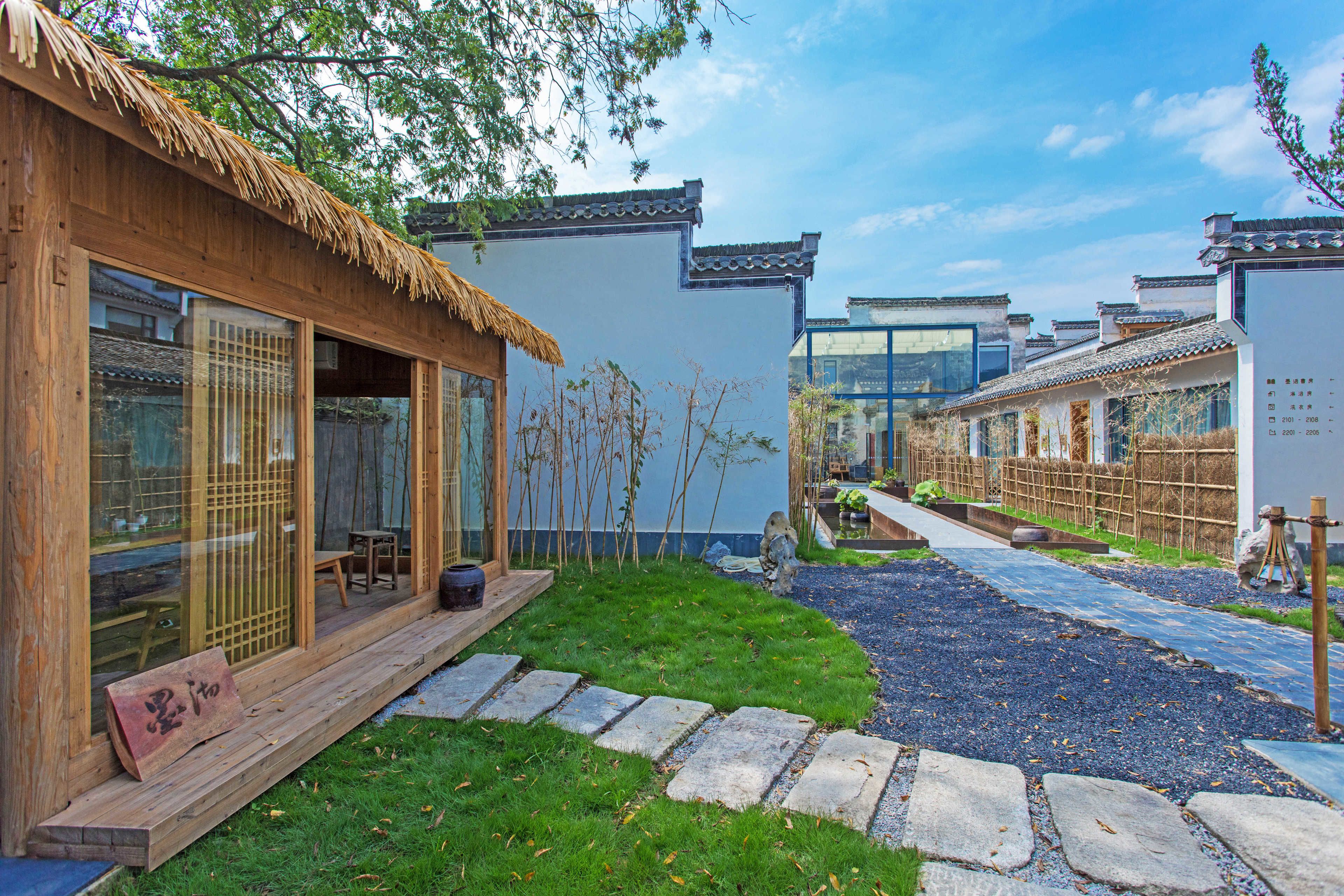 A traditional Japanese-style building with a thatched roof, wooden floors, and a stone pathway leading to a wooden deck.
