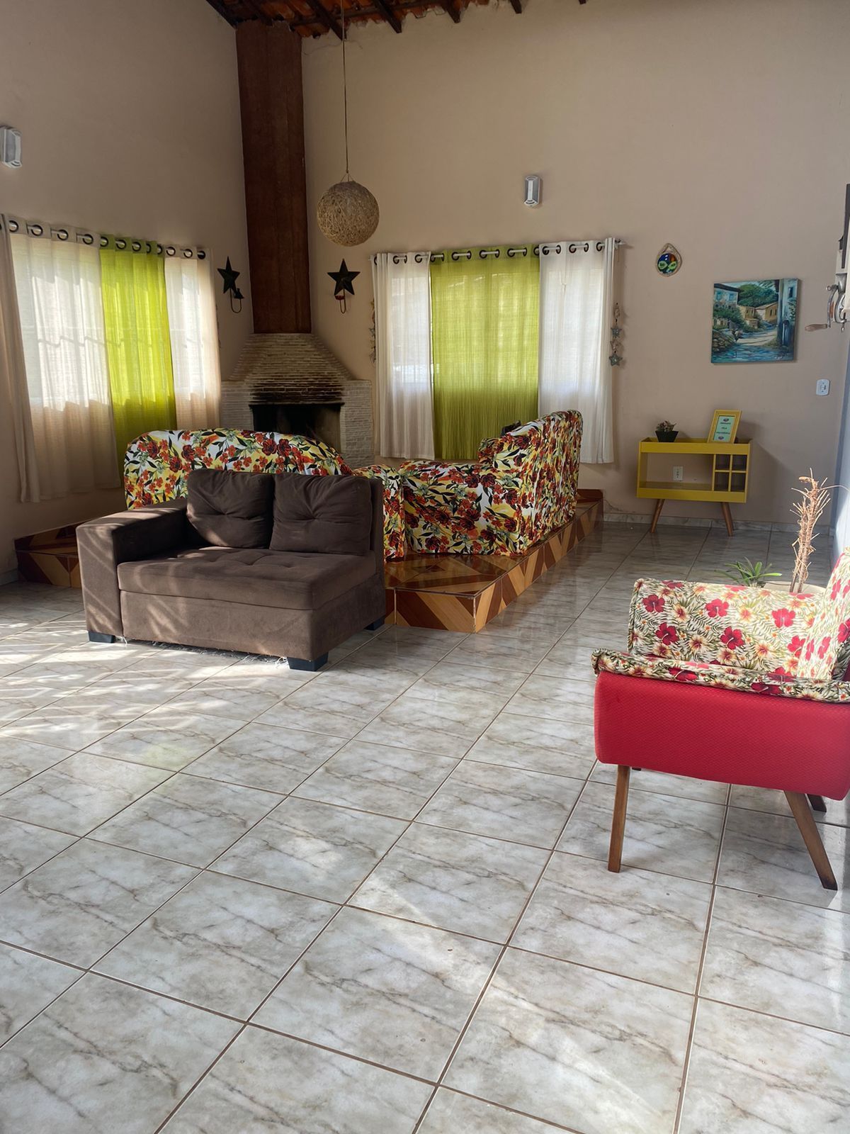 A living room with a sofa, armchairs, and a red chair. There is a fireplace, a yellow side table, and a painting on the wall.