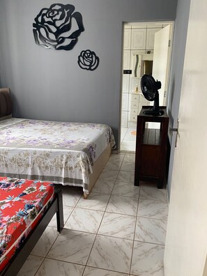 Ein Schlafzimmer mit einem Bett, einem Schminktisch, einem Ventilator und einer Wand mit Rosenmuster.