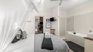 A bedroom with a bed, a bedside table, a mirror, a shower, and a fireplace in the background.