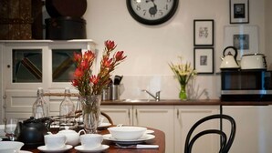 A dining area with a table set for four, a clock on the wall, and kitchen appliances in the background.