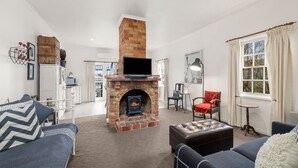 A living room with a brick fireplace, a television mounted above it, and a cozy seating area with a sofa and armchair.