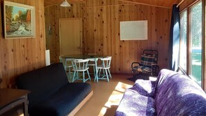 A cabin interior with wooden walls, a dining table with chairs, a sofa, and a rocking chair. - Algonquin Cabin on the Magnetawan river (Emsdale)
