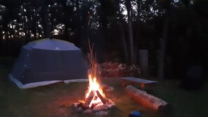 A tent, a campfire, and logs in a grassy area. - Algonquin Cabin on the Magnetawan river (Emsdale)