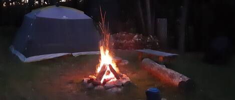 Une tente, un feu de camp et des bûches dans un espace herbeux.