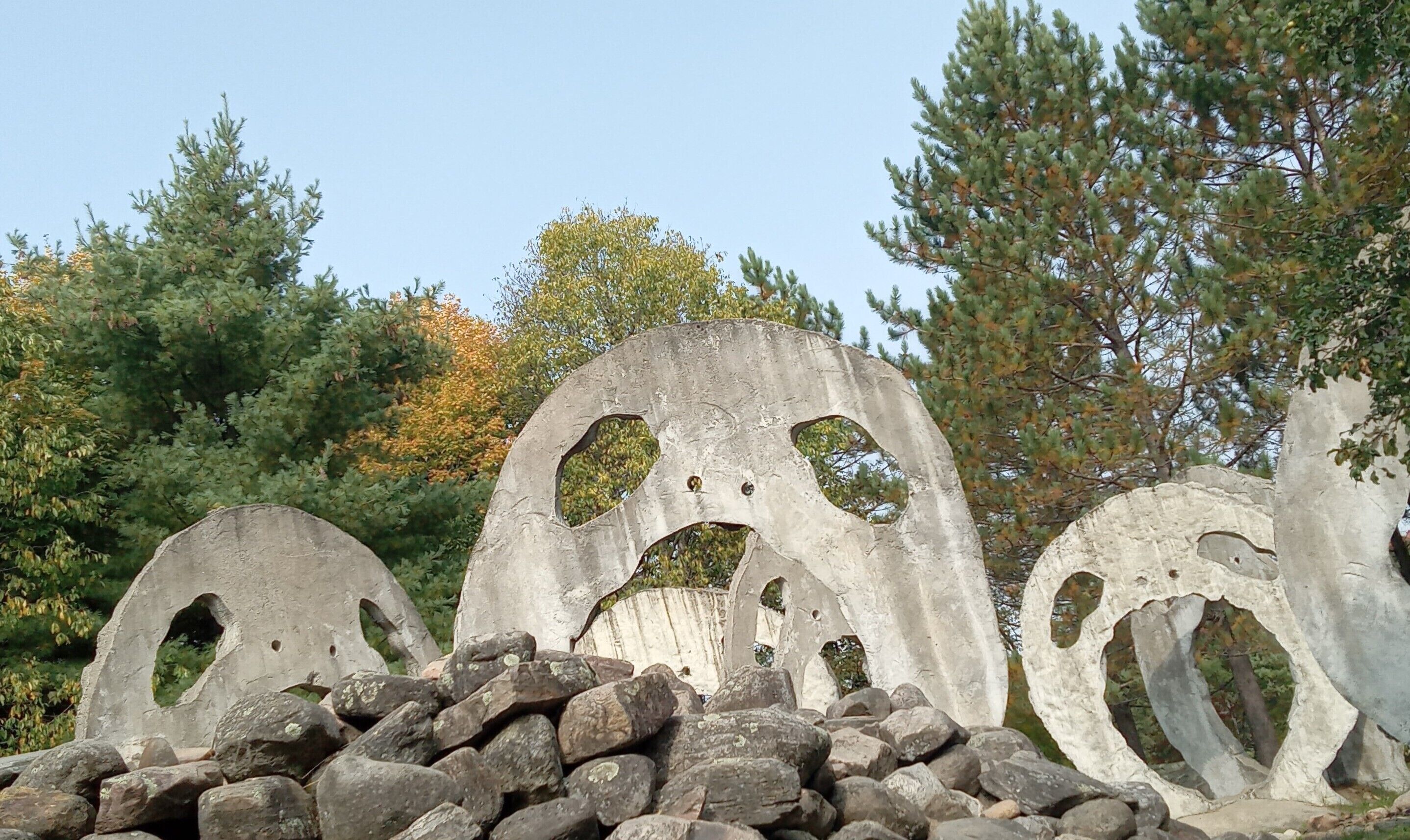 A pile of large, weathered concrete structures with circular cutouts, surrounded by rocks and trees.