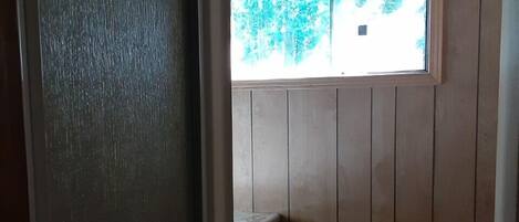 A small bathroom with a window, wooden walls, a toilet, and a sink.