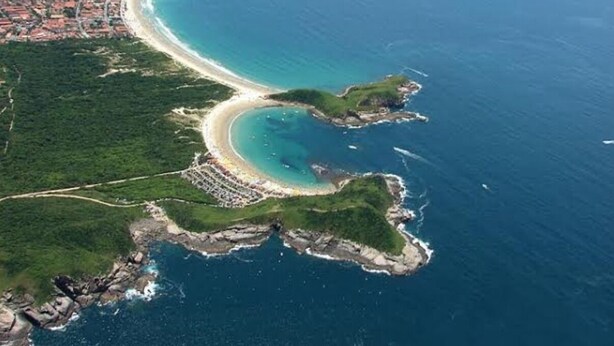 An aerial view of a coastal area with a curved bay, a beach, and a small peninsula with greenery.
