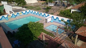A swimming pool with a wavy blue border, surrounded by greenery and a small building.