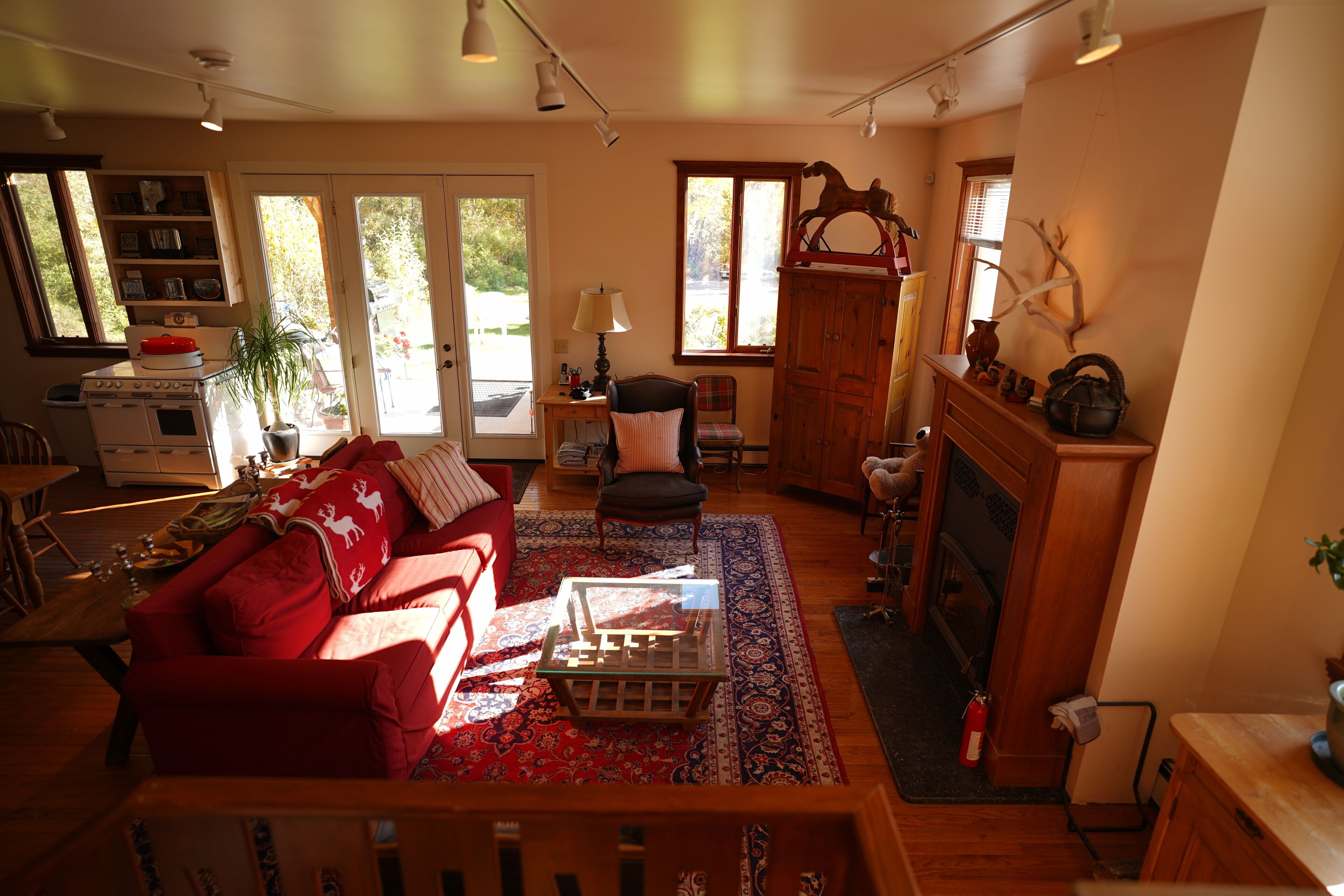 A cozy living room with a red sofa, a coffee table, and a fireplace. There is a wooden cabinet and a chair in the corner.