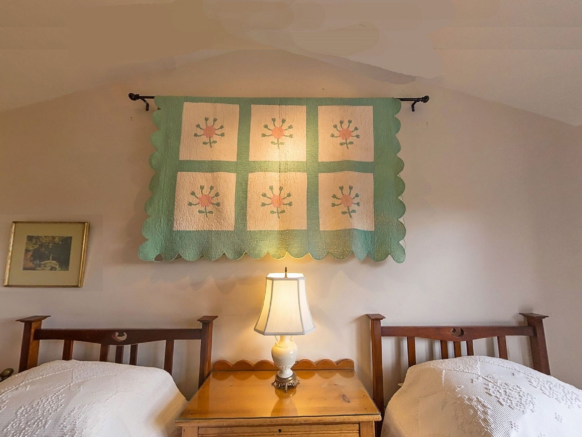 Een kamer met twee houten bedden, een nachtkastje met een lamp, en een groene quilt aan de muur.