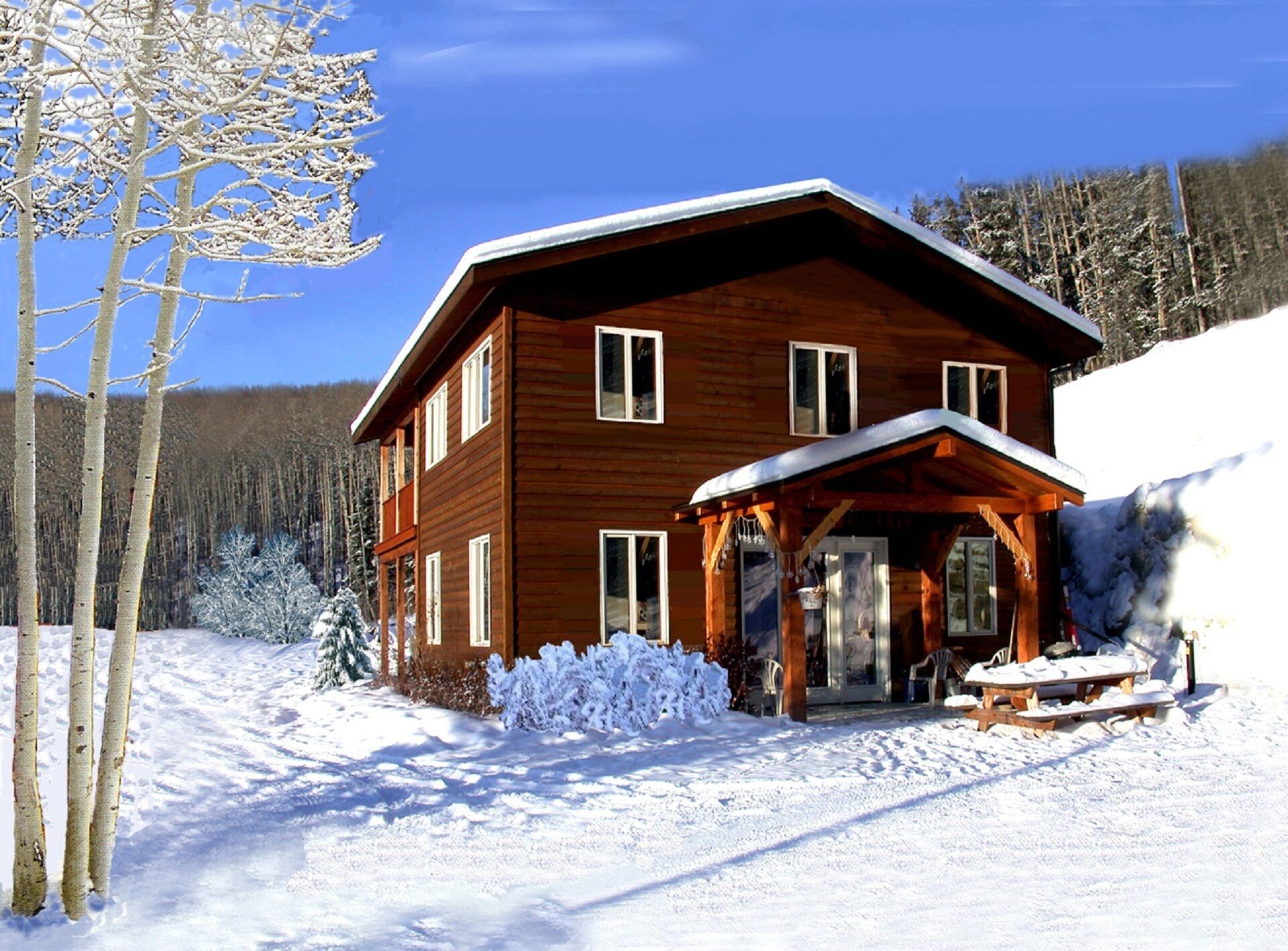 Een houten chalet met twee verdiepingen en een overdekte veranda, met een besneeerd landschap.