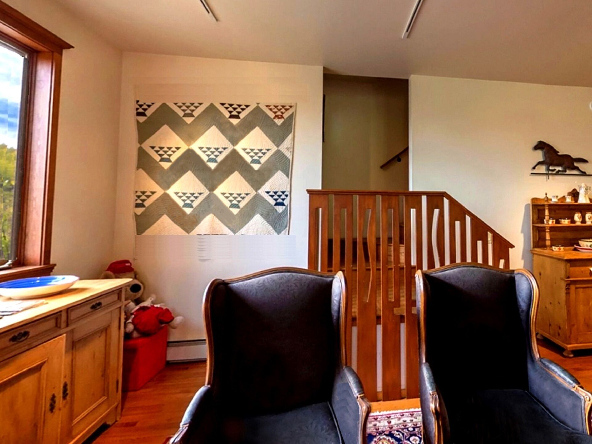 A room with two black armchairs, a wooden staircase, a patterned wall, and a wooden cabinet.