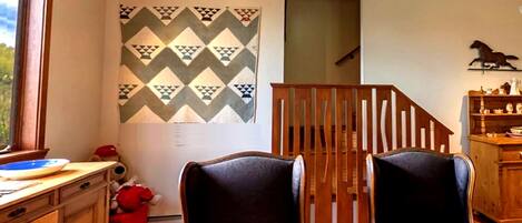 A room with two black armchairs, a wooden staircase, a patterned wall, and a wooden cabinet.