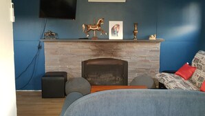 A room with a brick fireplace, a mounted television, and a patterned sofa with a red pillow. - Lockleigh Park - Escape to the Country (Lebrina)