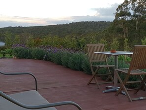 A patio with two wooden chairs and a table, surrounded by lush greenery and purple flowers. - Lockleigh Park - Escape to the Country (Lebrina)