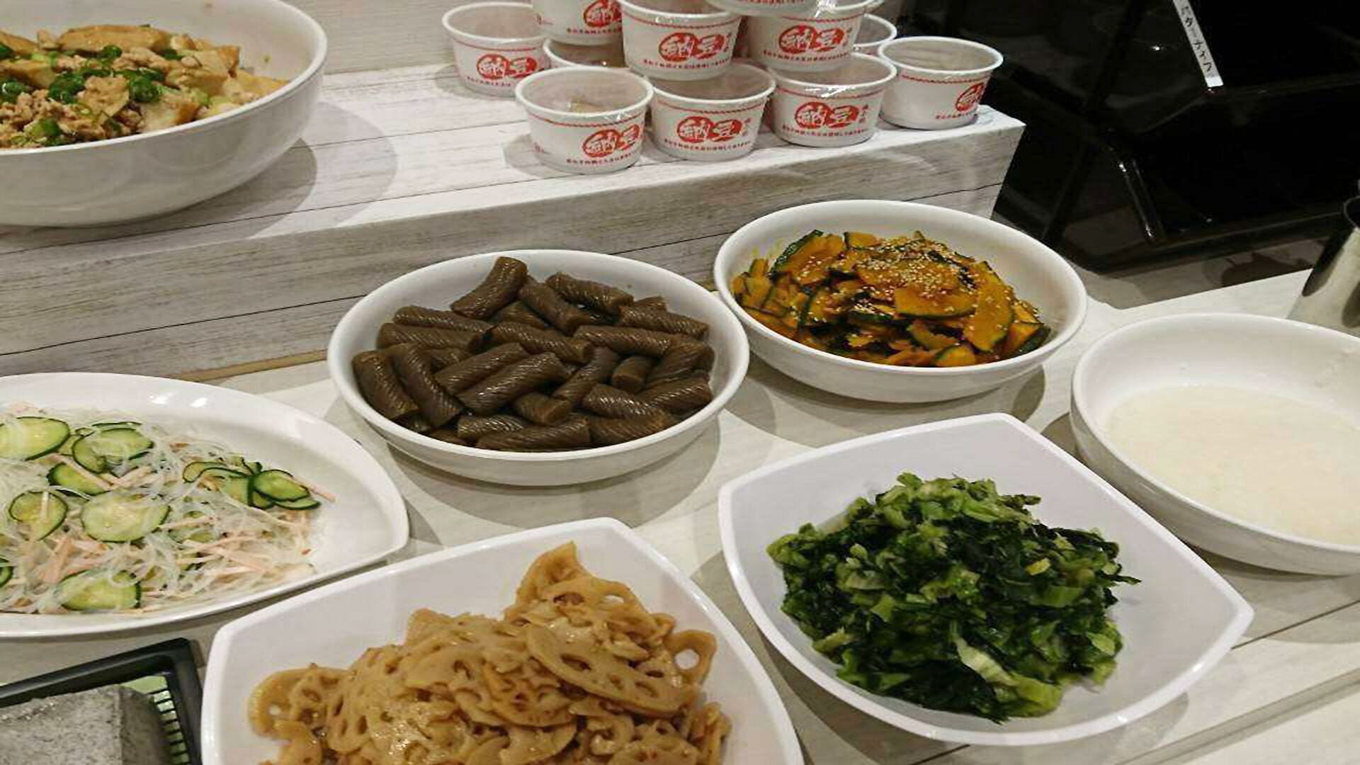 A variety of dishes on a table, including noodles, vegetables, and a bowl of soup.