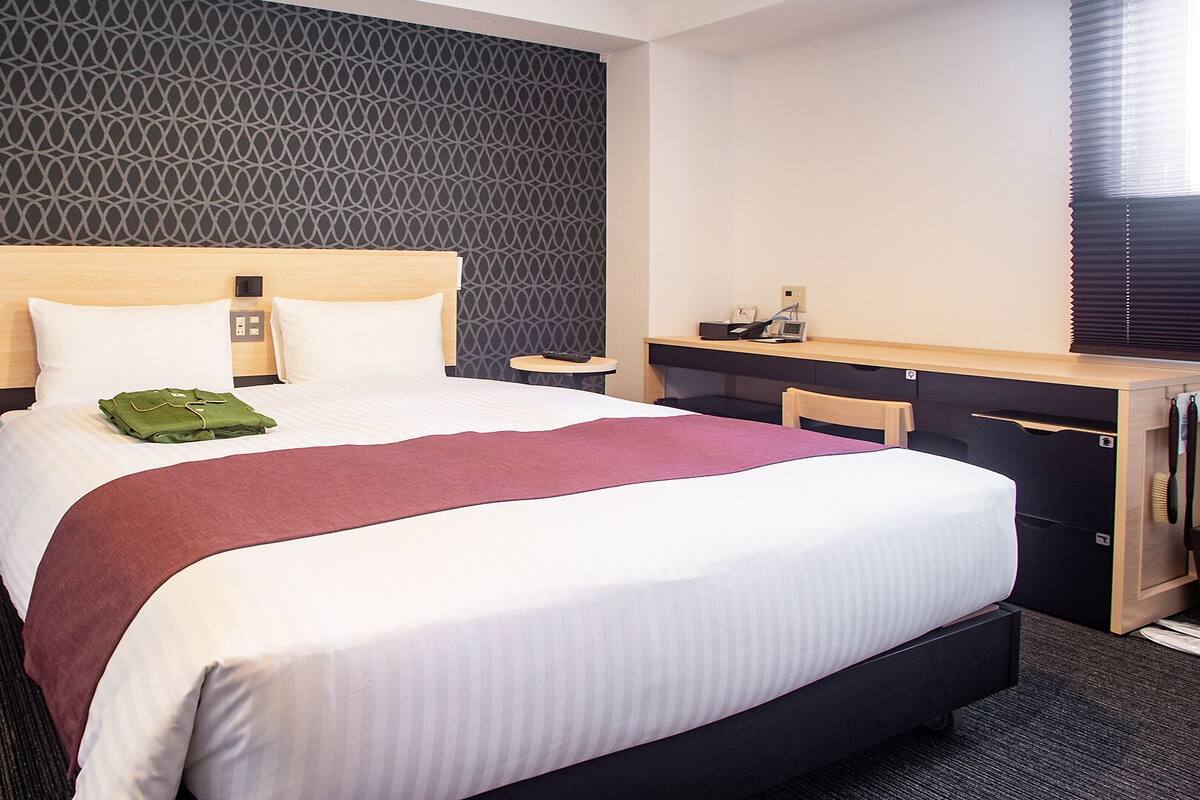 A hotel room with a large bed, a desk, and a chair.
