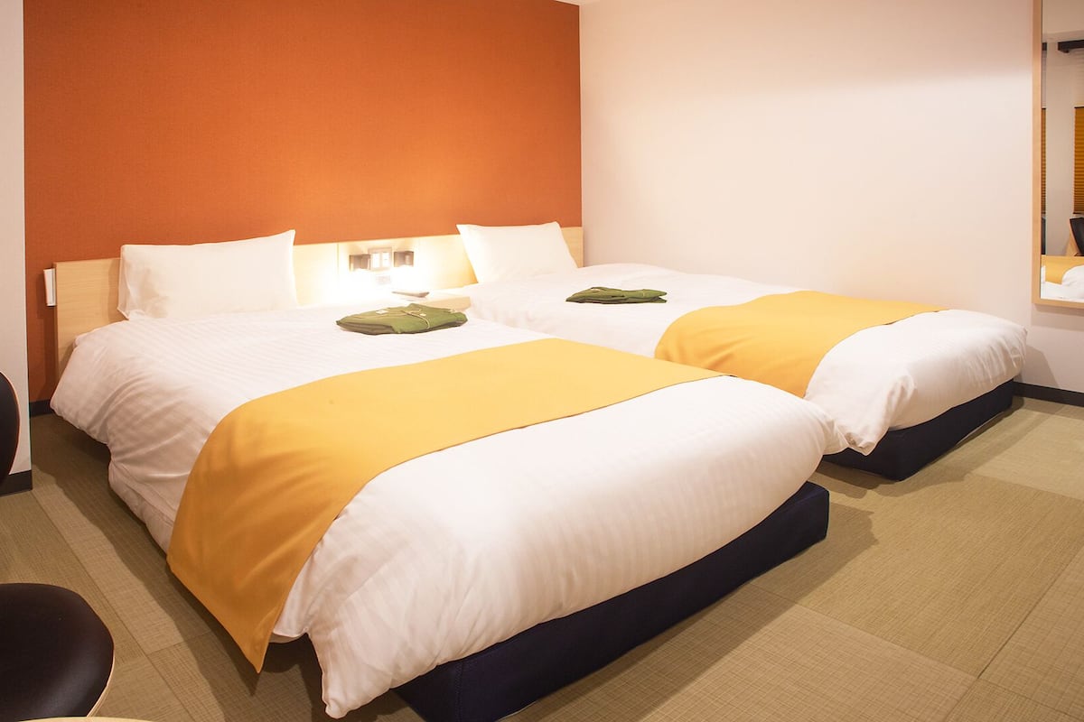 A hotel room with two beds, a desk, and a chair.