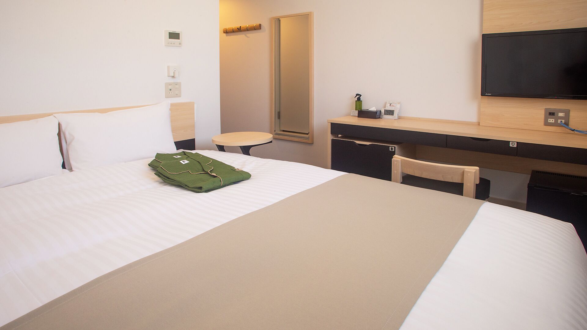 Habitación de hotel con cama, escritorio, silla, espejo, televisor y una mesita.