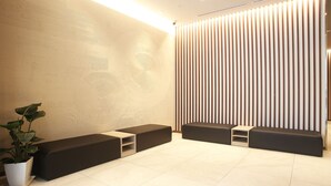 A modern waiting area with a textured wall, a vertical slat wall, and a potted plant. - Hotel Kuretakesou Hiroshima Otemachi (Hiroshima)