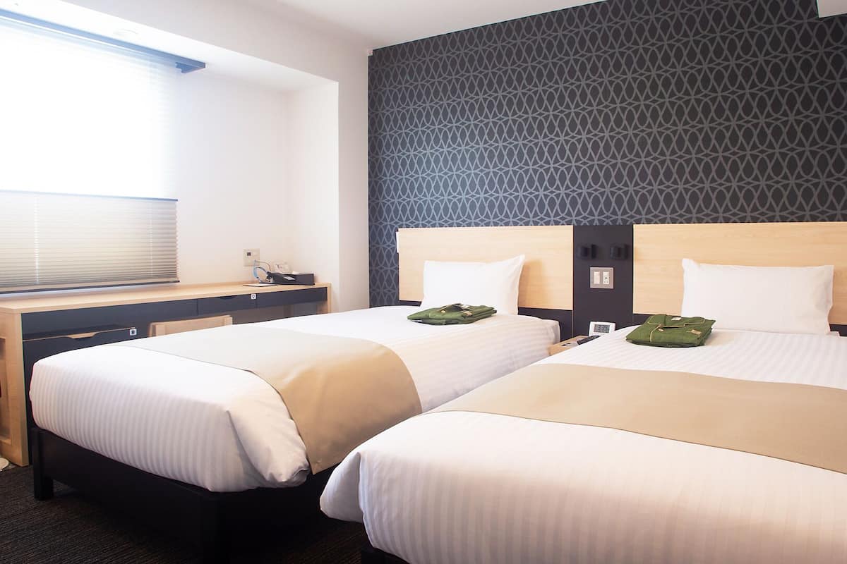 A hotel room with two beds, a desk, and a patterned wall.
