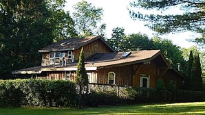 A two-story wooden house with a large front porch and a fenced yard.