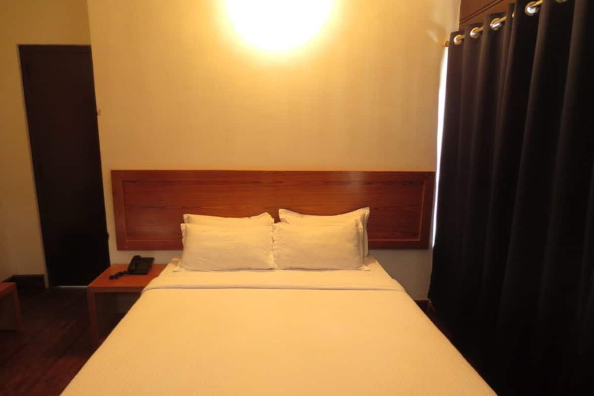 A hotel room with a large bed, a wooden headboard, a bedside table with a phone, and a curtain on the window.