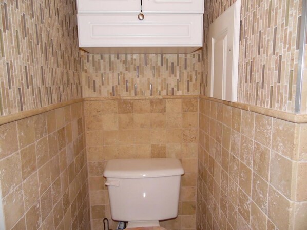 A bathroom with a toilet, tiled walls, and a white cabinet above the toilet. - SUNSET VIEWS-Pristine WATERFRONT Penthouse Condo on SML- Boat Slip Available (Moneta)