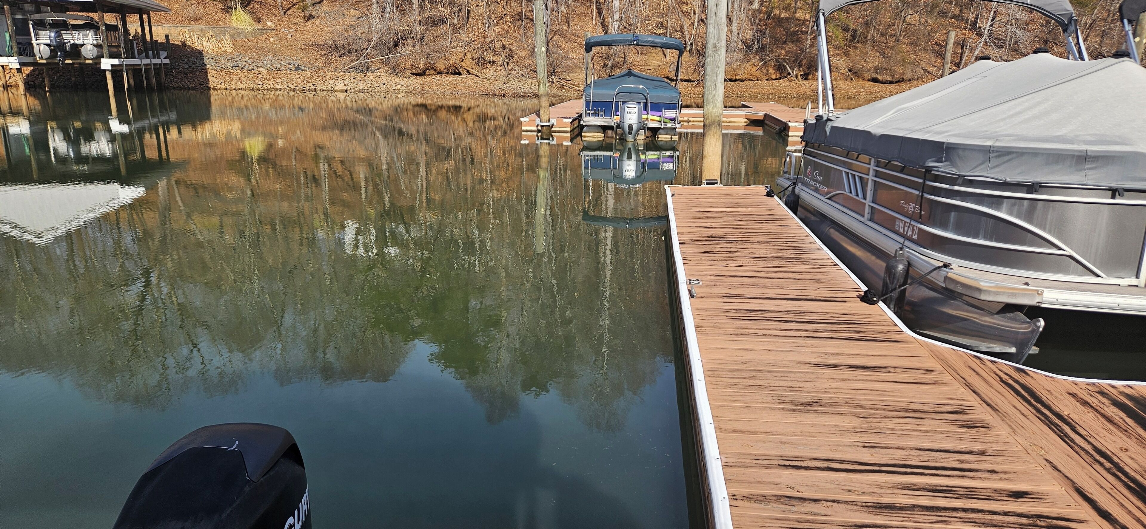 A docked boat with a covered trailer and a wooden dock extending into a calm body of water.