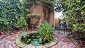 Un jardin avec un chemin en briques, un étang parsemé de nénuphars et une clôture en bois.