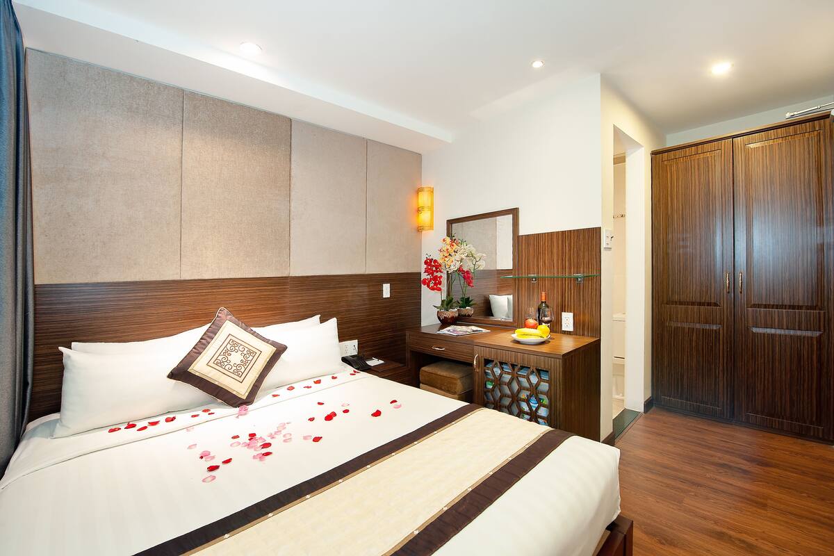A hotel room with a large bed, a wooden headboard, a nightstand, a desk with a mirror, and a wardrobe.