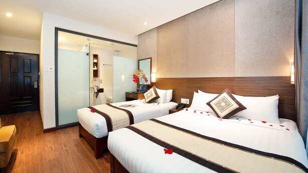 A hotel room with two beds, a wooden floor, a large mirror, and a door leading to a bathroom. - Saigonciti Hotel (Ho Chi Minh City)
