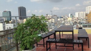 A rooftop terrace with tables and chairs, a potted plant, and a cityscape view. - Saigonciti Hotel (Ho Chi Minh City)