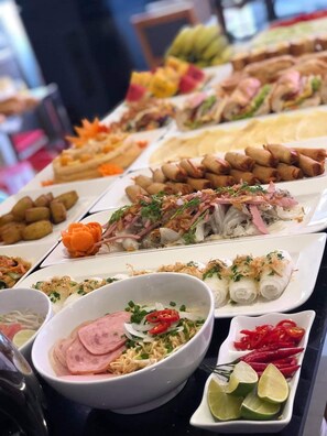 Un bufé con diversos platos, entre ellos rollitos primavera, fideos y carnes en rodajas.
