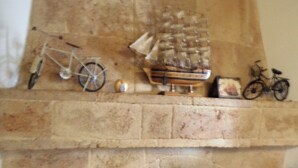 Une cheminée en pierre avec un manteau en briques, une petite arche et une étagère au-dessus où sont disposés divers objets, notamment un vélo, un panier et un tableau encadré.