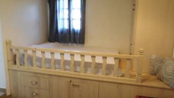 Quarto com estrutura de cama de madeira, janela com cortinas, mesa de cabeceira e tapete listrado.