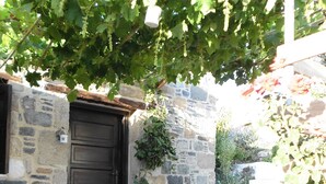 Un bâtiment en pierre avec une porte en bois sombre, un pot de fleurs, une table avec des chaises et un sol en pierre.