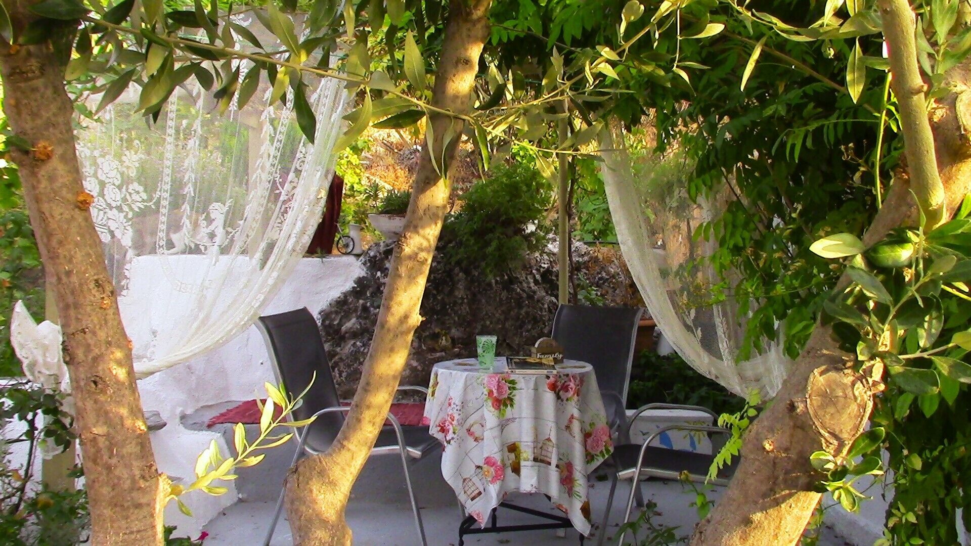 Ein Sitzbereich im Freien mit einem Tisch, der mit einer blumigen Tischdecke bedeckt ist, umgeben von Stühlen und mit weißem Stoff drapiert.