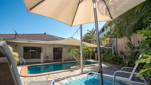 Ein Garten mit Swimmingpool, Liegestühlen und einer überdachten Terrasse.