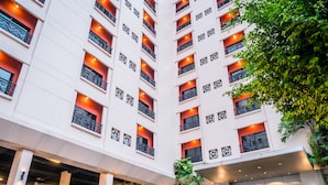 A multi-story hotel with a modern design, featuring balconies with decorative railings, a covered entrance, and a parking area with several cars. - Atrium Boutique Hotel (Bangkok)