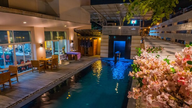 An indoor pool area with a wooden deck, seating, and a water feature. - Atrium Boutique Hotel (Bangkok)
