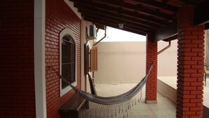 A covered outdoor area with a hammock, brick walls, and a tiled floor. - House with pool, barbecue, air conditioning. (Caraguatatuba)