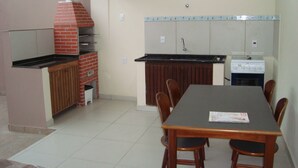 A kitchen with a brick oven, a sink, a stove, and a dining table with chairs. - House with pool, barbecue, air conditioning. (Caraguatatuba)