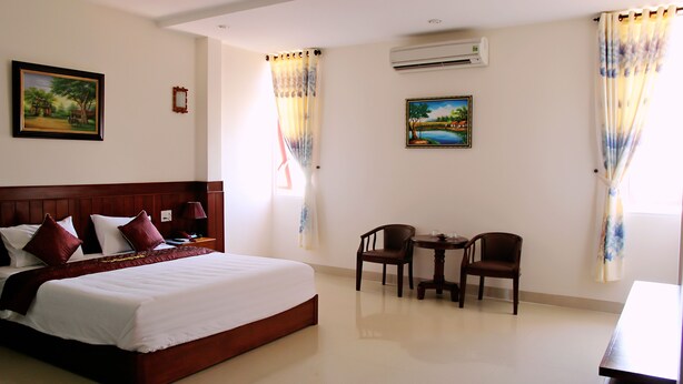 A hotel room with a large bed, two chairs, a small table, and two paintings on the walls. - Tram Huong (Da Nang)