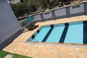A swimming pool with stone tiles, a lounge chair, and an umbrella.